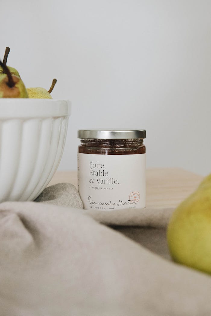 Gourmet jar with pear, maple, and vanilla flavors next to a bowl of fresh pears.